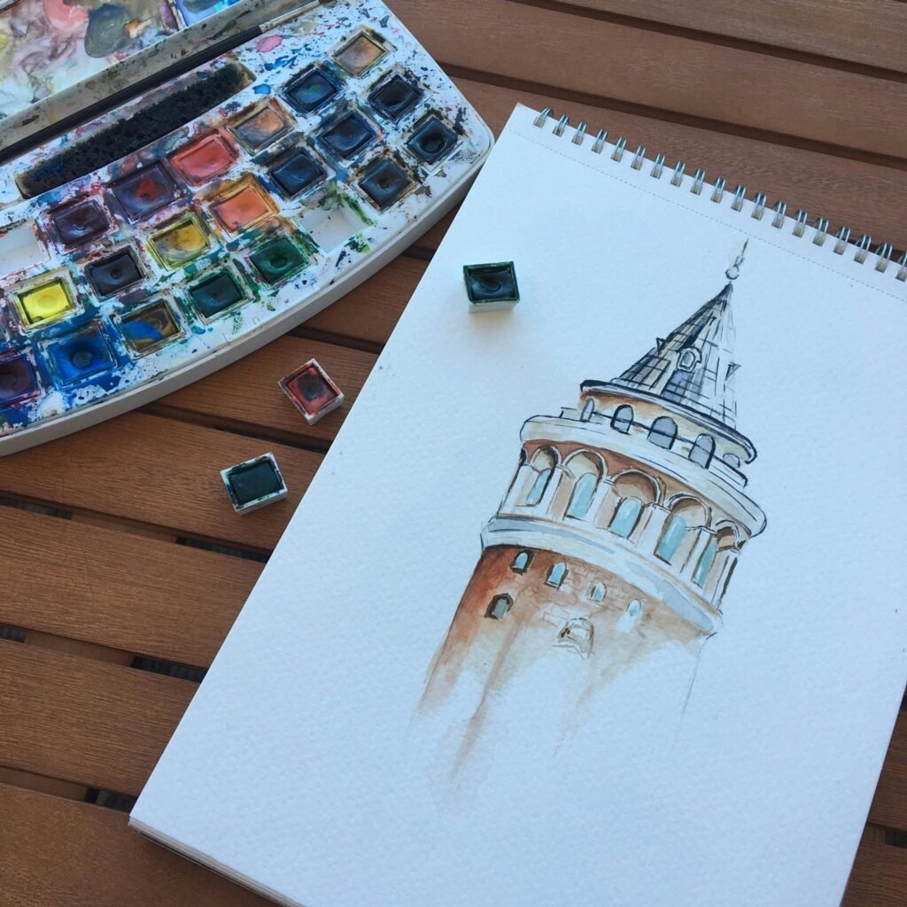 Artistic watercolor sketch of Galata Tower with palette on wooden surface, inspiring creativity.